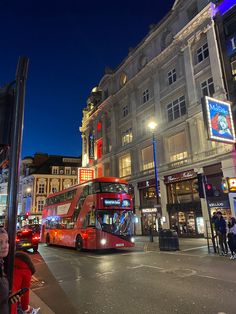 a red double decker bus driving down a street next to tall buildings and traffic lights