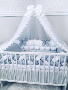 a baby crib with white bedding and blue pillows on the bottom, in front of a wall