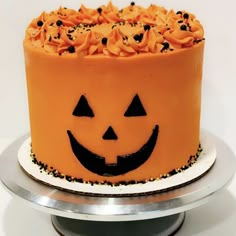 a halloween cake decorated with orange icing and black sprinkles on a silver platter