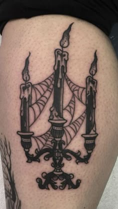 a black and white photo of a candle tattoo on the thigh, with two candles