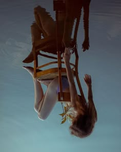 a woman floating in the water with her legs up on a chair that is suspended upside down