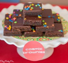 chocolate brownies with sprinkles are on a cake platter that says cosmic brownies