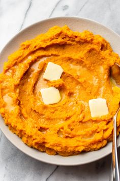 a white bowl filled with mashed sweet potatoes and topped with butter cubed cheese