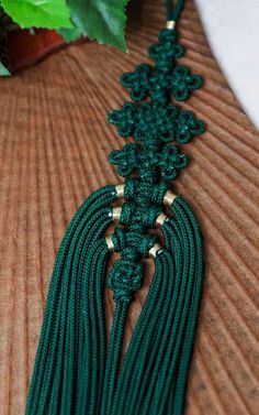 a green tasseled necklace with gold accents on a table next to a potted plant