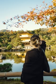 a woman standing next to a lake in front of a building