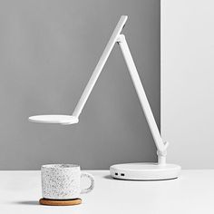 a white desk lamp sitting on top of a table next to a cup and saucer