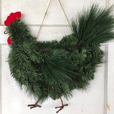 a chicken made out of pine branches hanging on a door frame with red felt flowers