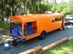 an orange school bus parked on the side of the road next to some cars and trees