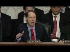 a man in a suit and tie sitting at a table with other people behind him