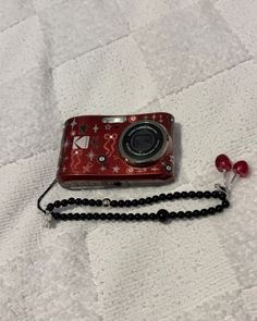 a red camera sitting on top of a white bed next to a black beaded necklace