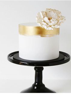 a white and gold decorated cake sitting on top of a black plate with a golden flower