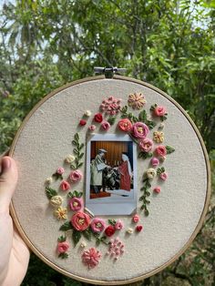 a person holding up a embroidery project with pink flowers and an image of a man in a suit