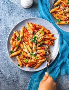 two plates of pasta with sauce and parmesan cheese on them, next to a blue towel