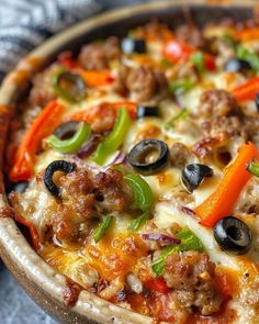 a pizza with cheese, olives, peppers and meat in a wooden bowl on a table