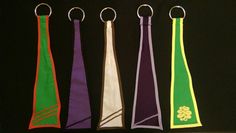 four different colored ties hanging from hooks on a black background with the same color ribbon attached to them