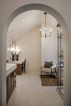 an arched doorway leads to a bathroom with a sink and tub in the corner, while a chair sits at the end of the room