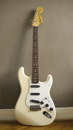 an electric guitar sitting on top of a hard wood floor next to a gray wall