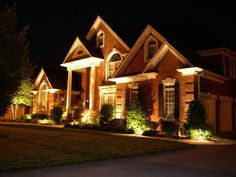 a house lit up at night with lights in the front yard and landscaping around it