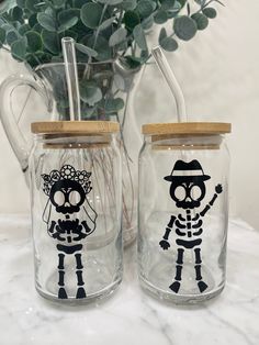 two mason jars decorated with skeleton images and straws are sitting on a table next to a potted plant