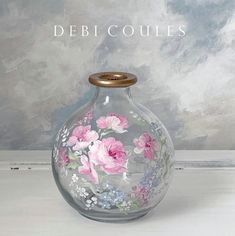 a glass vase with pink flowers painted on it and the words debicoulies above it