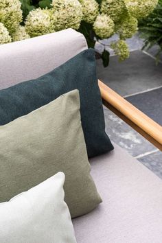 four pillows sitting on top of a white couch next to green and white hydrangeas