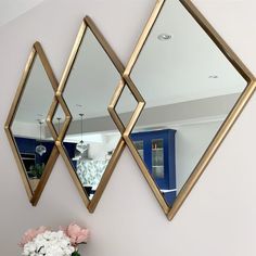 two mirrors are hanging on the wall next to a vase with white flowers in it