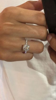 a woman's hand holding a cell phone with a diamond ring on her finger