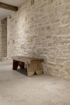 a bench sitting in front of a stone wall next to a wooden beam on the floor