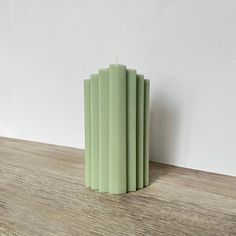 a small green candle sitting on top of a wooden table next to a white wall