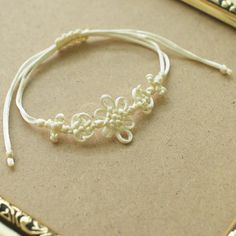 there is a white string bracelet that has beads on it and a gold frame around it