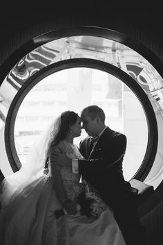 a bride and groom kissing in front of a circular window