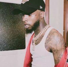 a man with tattoos wearing a red tie and a baseball cap standing in front of a wall