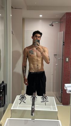 a shirtless man standing in front of a bathroom sink taking a selfie with his phone