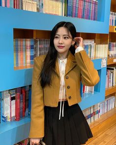 a girl in a school uniform is standing by a book shelf and holding a purse