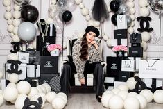 a woman is sitting on a chair surrounded by balloons and gift bags in front of her