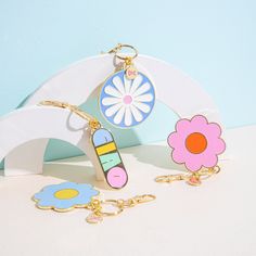 two key chains with flower charms attached to them sitting on a white table next to a blue wall