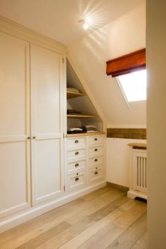 an attic bedroom with white cupboards and wooden flooring, built in to the wall