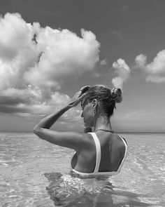 a woman standing in the ocean with her hands on her head and looking into the distance