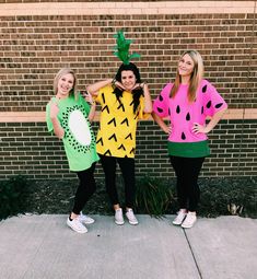 three women in costumes standing next to a brick wall