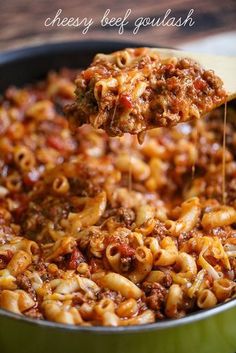 a wooden spoon full of macaroni and cheese being lifted from a skillet