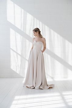 a woman standing in a white room wearing a strapless wedding dress with high low back