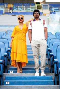 a man standing next to a woman in an orange dress on top of blue bleachers