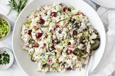 a white bowl filled with chicken salad next to two bowls of grapes and celery