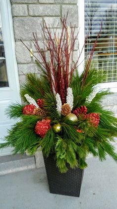 a planter filled with pine cones and red berries on the outside of a house