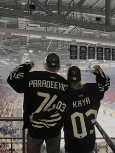 two people in black hockey jerseys looking at an arena