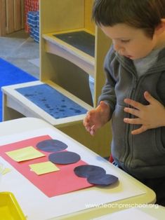 a young boy standing in front of a table with paper cutouts and scissors on it