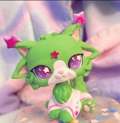 a green cat figurine sitting on top of a small table next to a purple blanket