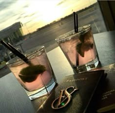 two glasses filled with drinks sitting on top of a wooden table next to a book