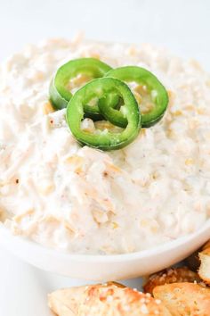 a white bowl filled with dip next to crackers and jalapenos