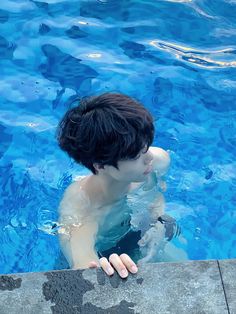 a young boy swimming in a pool with his hand on the edge of the water